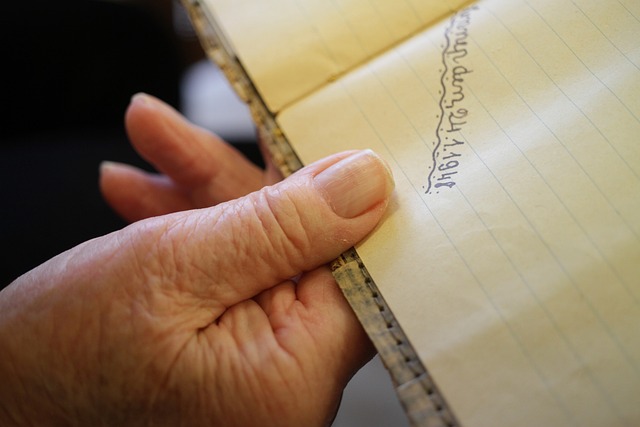 Hand writing with a fountain pen in an open notebook on a wooden desk with natural daylight
