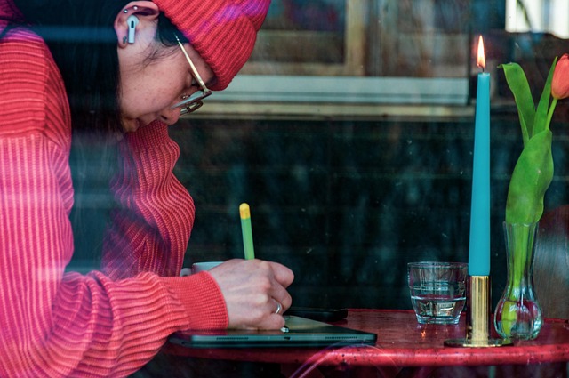 Person writing with concentration at a well-lit desk with notebook and pen visible